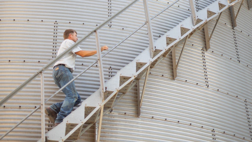 A man walking upstairs on the side of a corn silo. 