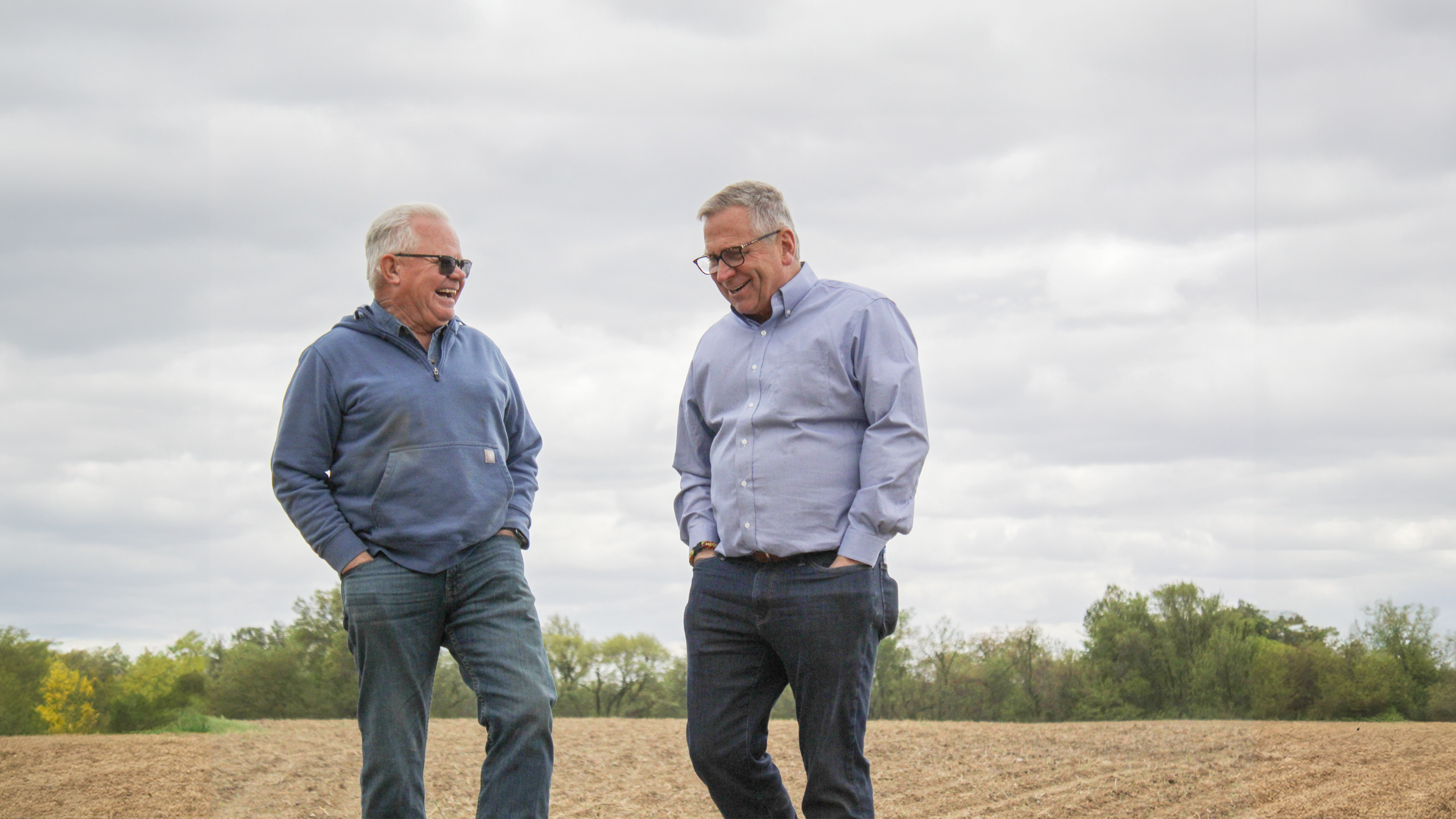 Two men talking at the edge of a harvested field on a gloomy day. 