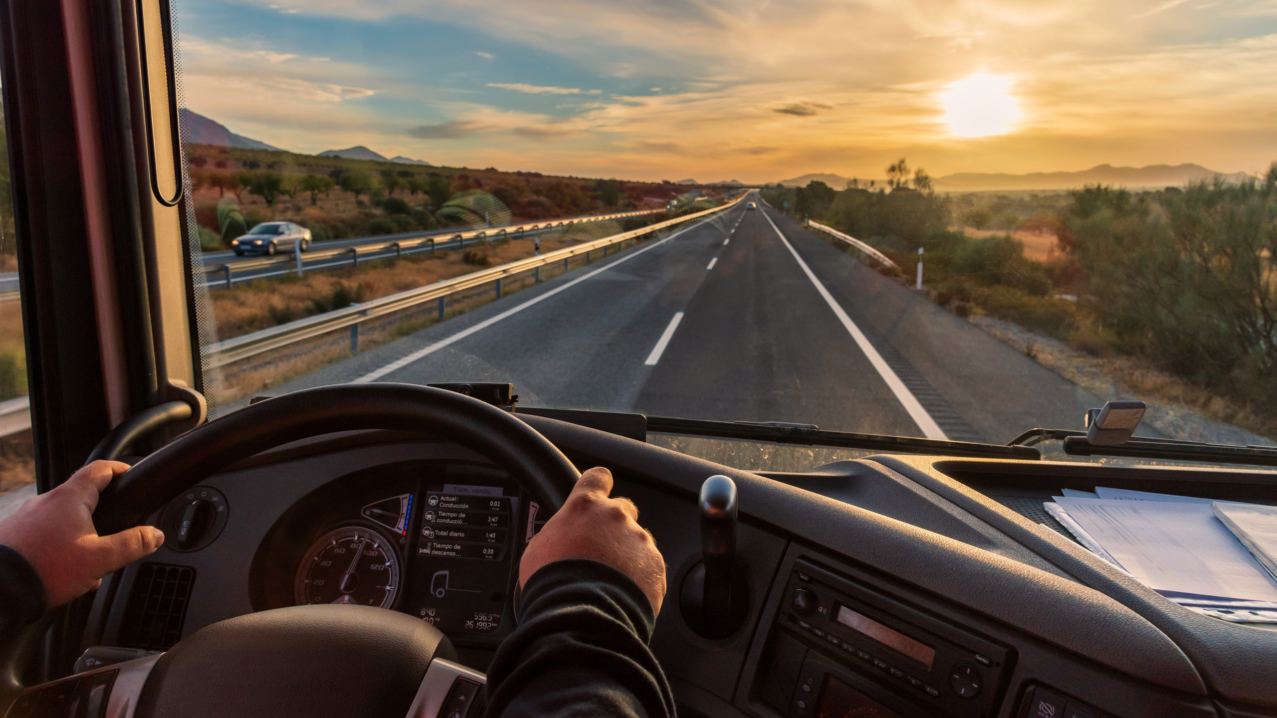 View of someone driving a semi truck from the inside looking out onto the highway at sunset.