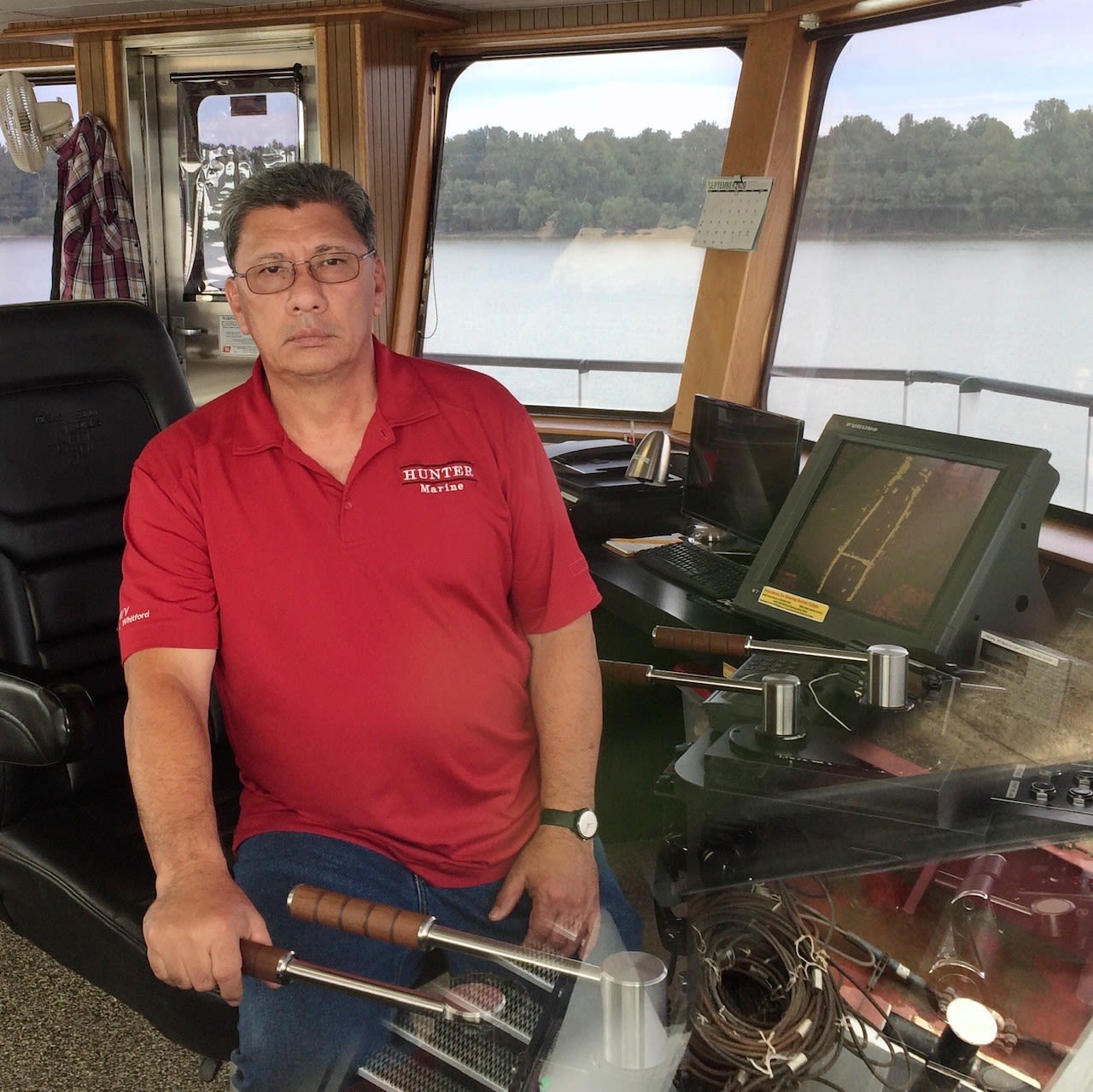 Image of Ray Bennett in a red shirt driving a river barge. 