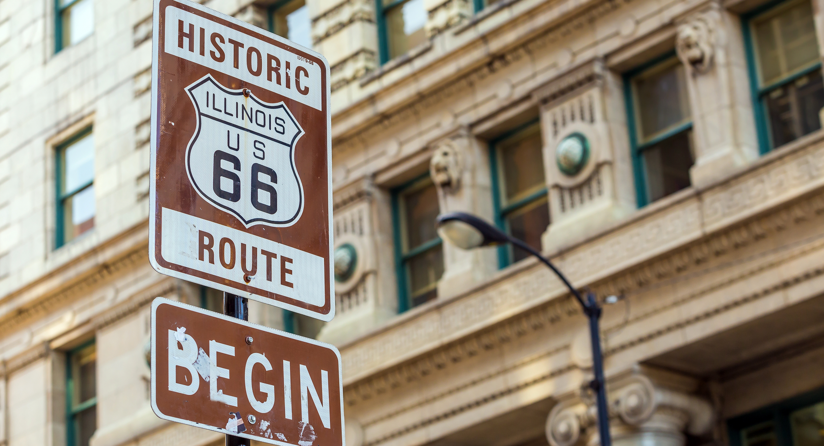 Brown Route 66 sign in front of a tan concrete building.
